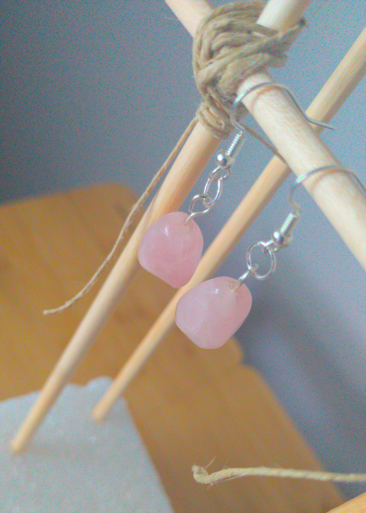 A top-down image of a pair of pink handmade earrings being displayed on a stand. There is an irregular shaped pink stone that is the focal piece of the earring. The hooks are a silver color.