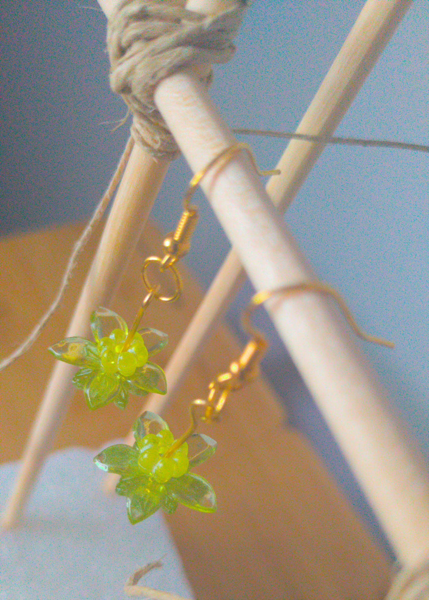A top-down image of a pair of green handmade earrings being displayed on a stand. There are three stacked beads that make up the earring. The first bead is a small yellow flower. The next bead is a larger green flower and the last is a flat flower. All beads are translucent. The hooks are a golden color.