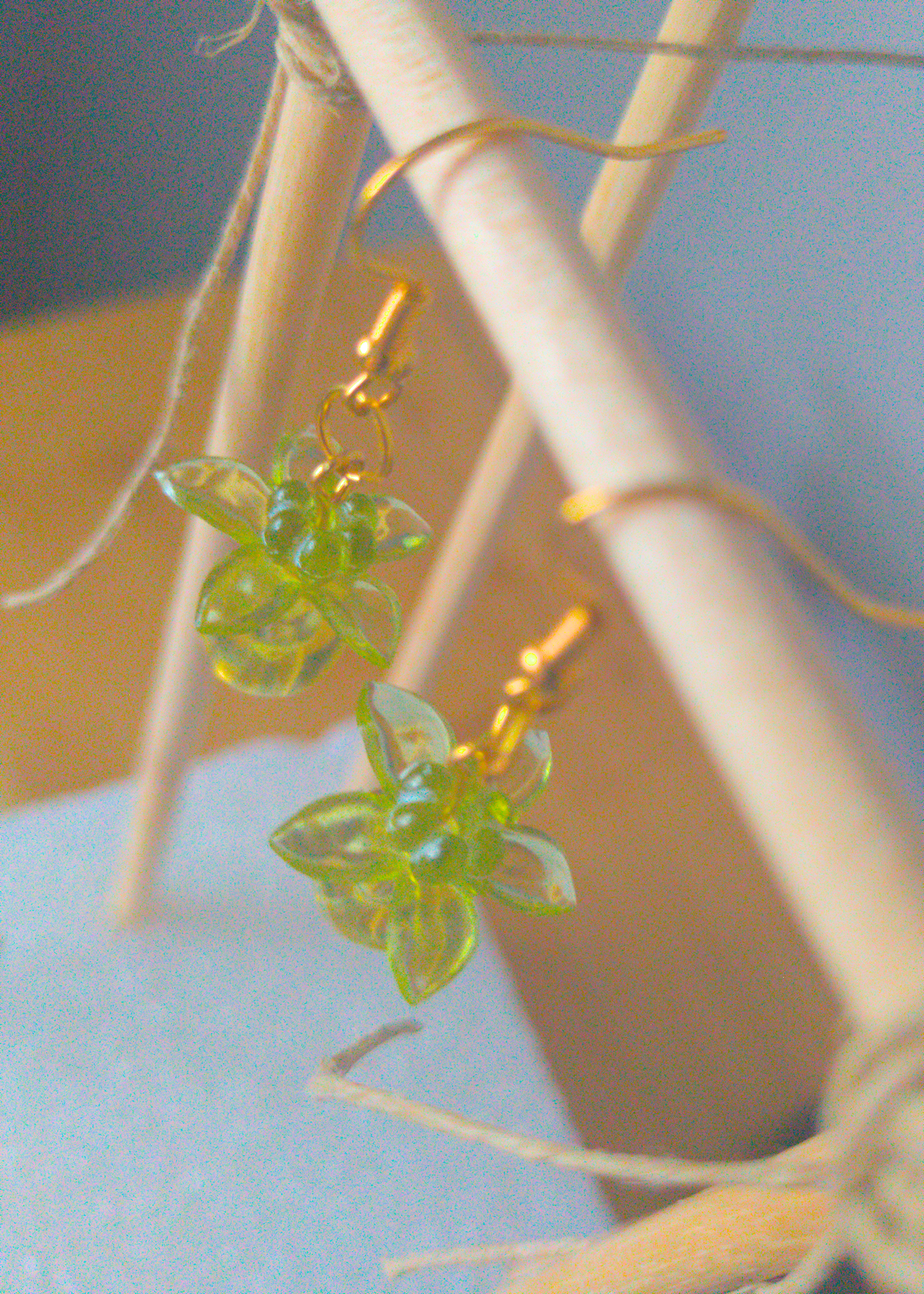 A top-down image of a pair of green handmade earrings being displayed on a stand. There are three stacked beads that make up the earring. The first bead is a small green flower. The next bead is a larger green flower and the last is a large ball. All beads are translucent. The hooks are a golden color.