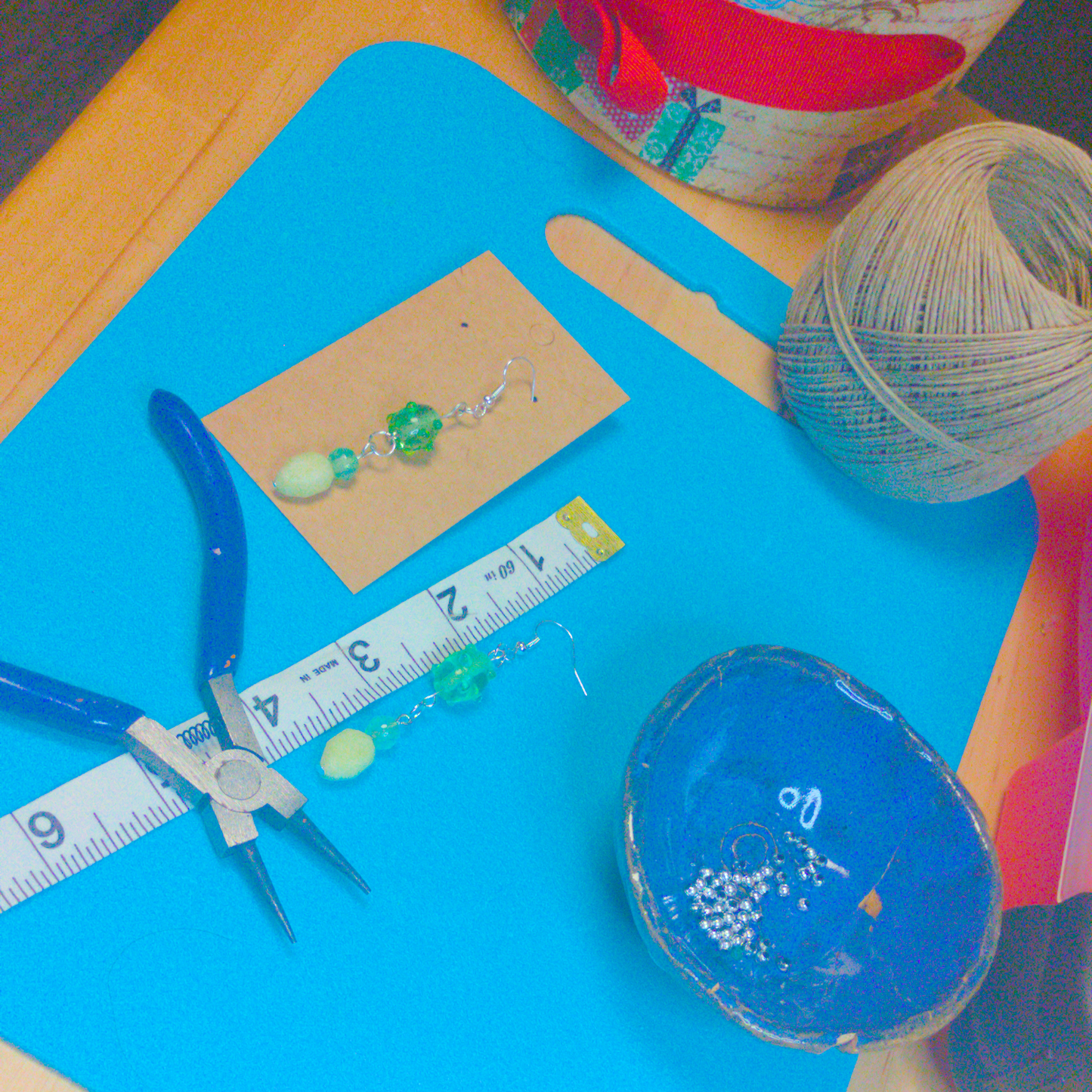 An image of a pair of green handmade earrings being measured on a work table. The pair is 2.75 inches long.