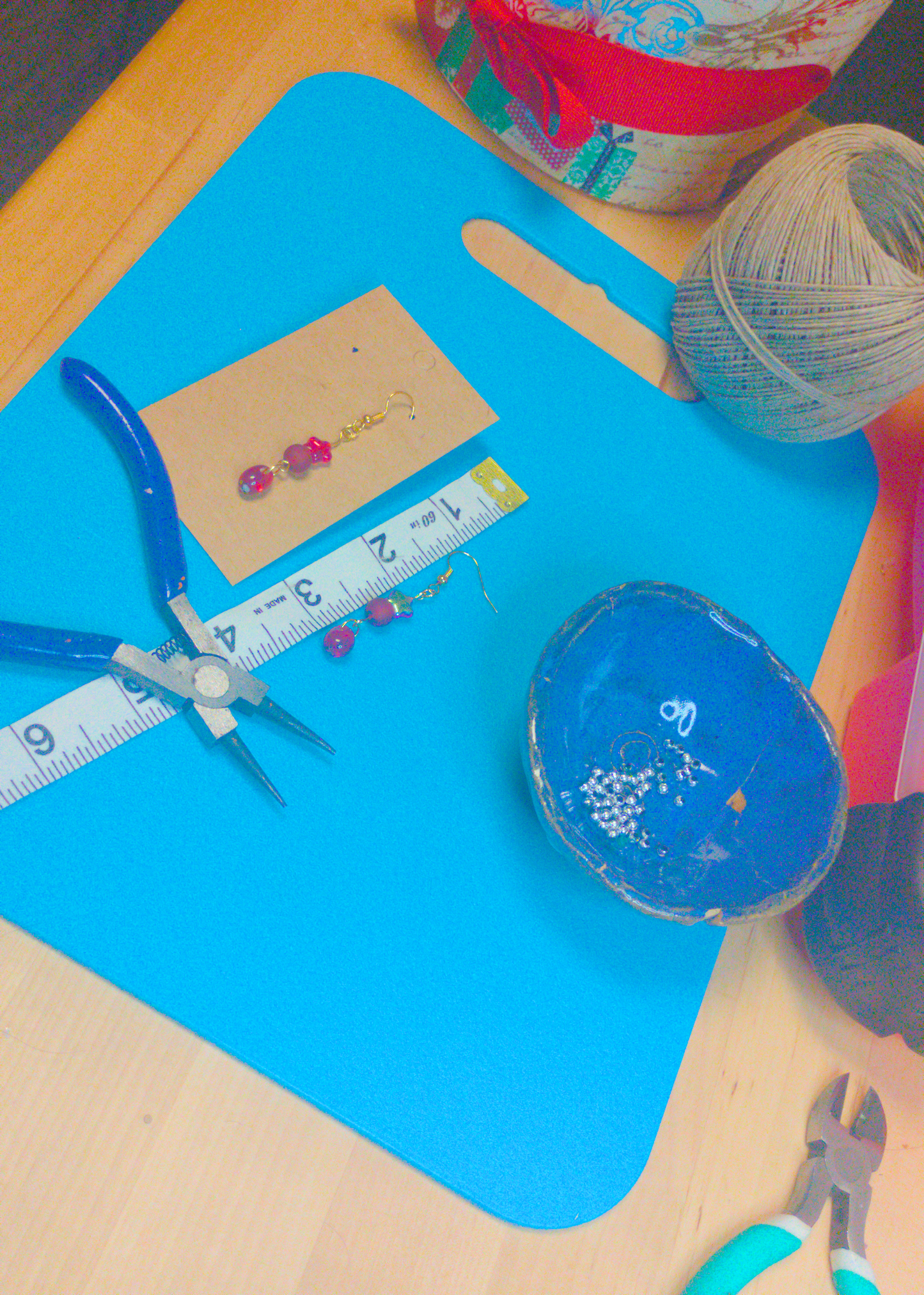 An image of a pair of red handmade earrings being measured on a work table. The pair is 2.25 inches long.