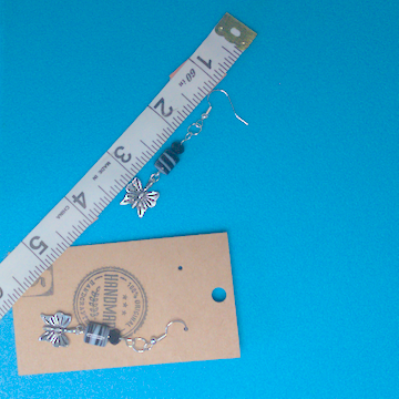A pair of black and silver earrings being measured on a work table. The pair is 2.5 inches long.