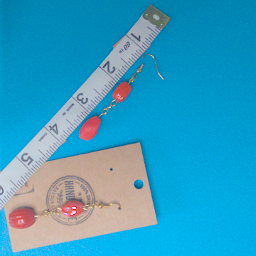 A pair of orange earrings being measured on a work table. The pair is 2.5 inches long.