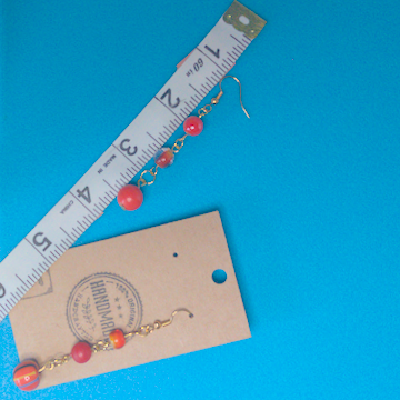 A pair of orange earrings being measured on a work table. The pair is 2.5 inches long.