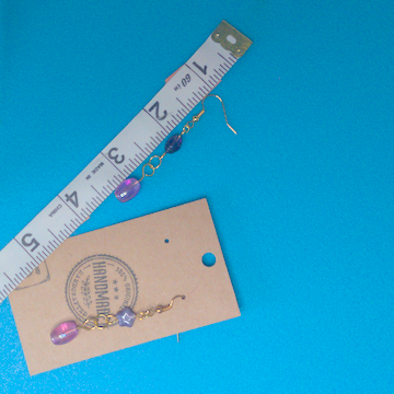 A pair of purple earrings being measured on a work table. The pair is 2.25 inches long.