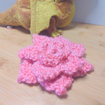 A pink crochet flower with four layers of petals. The layers are stacked flat on top of each other.