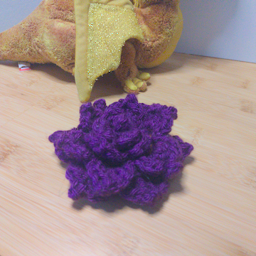 A purple crochet flower with four layers of petals. The layers are stacked flat on top of each other.