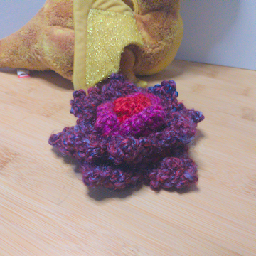A purple and red crochet flower with four layers of petals. The layers are stacked flat on top of each other.
