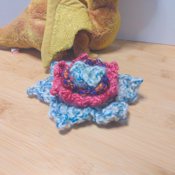 A white and pink crochet flower with four layers of petals. The layers are stacked flat on top of each other.