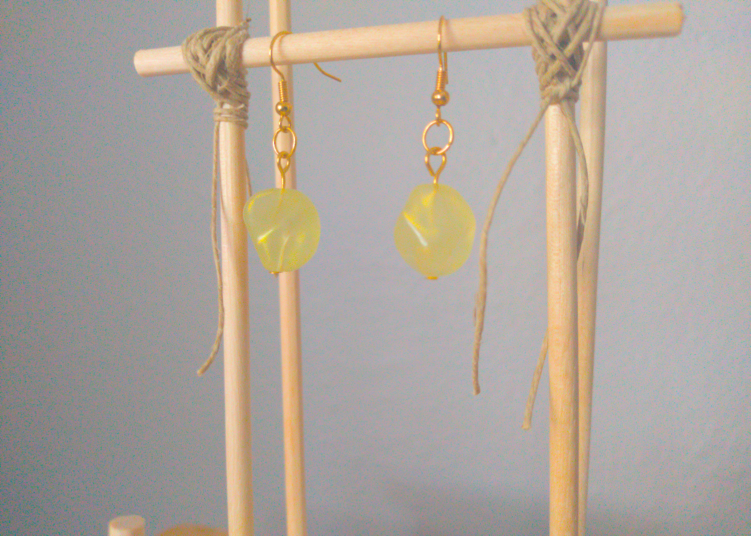 A front facing image of a pair of green handmade earrings being displayed on a stand. There is an irregularly shaped green bead with a gold shimmer that is the focal piece of the earrings. The hooks are a golden color.