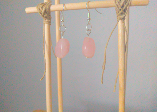 A front facing image of a pair of pink handmade earrings being displayed on a stand. There is an irregular shaped pink stone that is the focal piece of the earring. The hooks are a silver color.