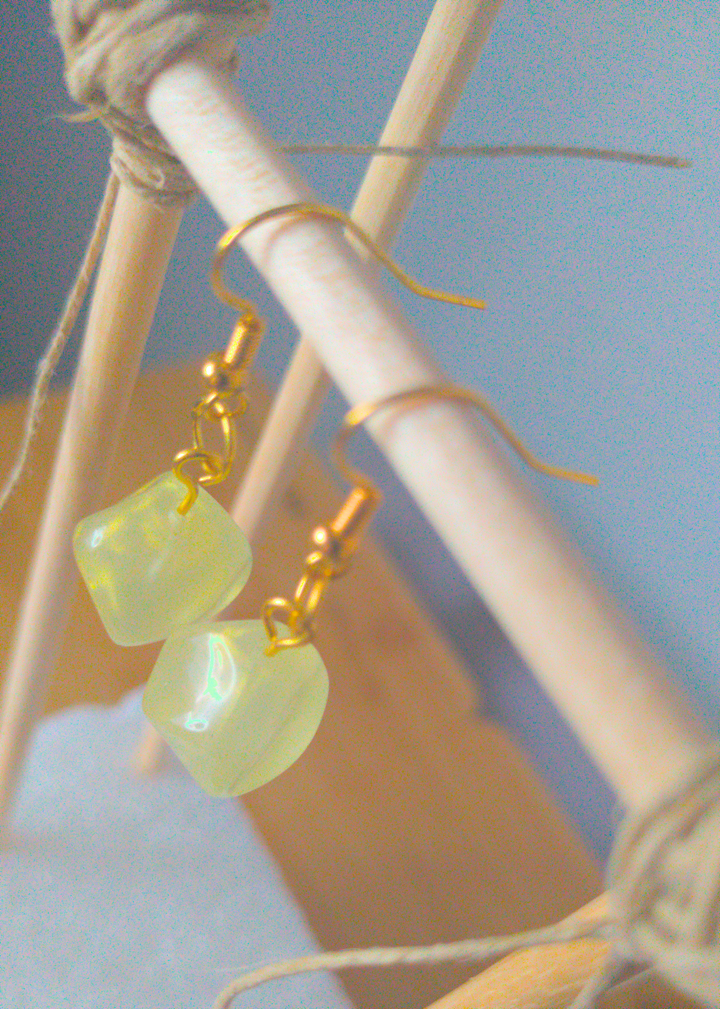 A top-down image of a pair of green handmade earrings being displayed on a stand. There is an irregularly shaped green bead with a gold shimmer that is the focal piece of the earrings. The hooks are a golden color.