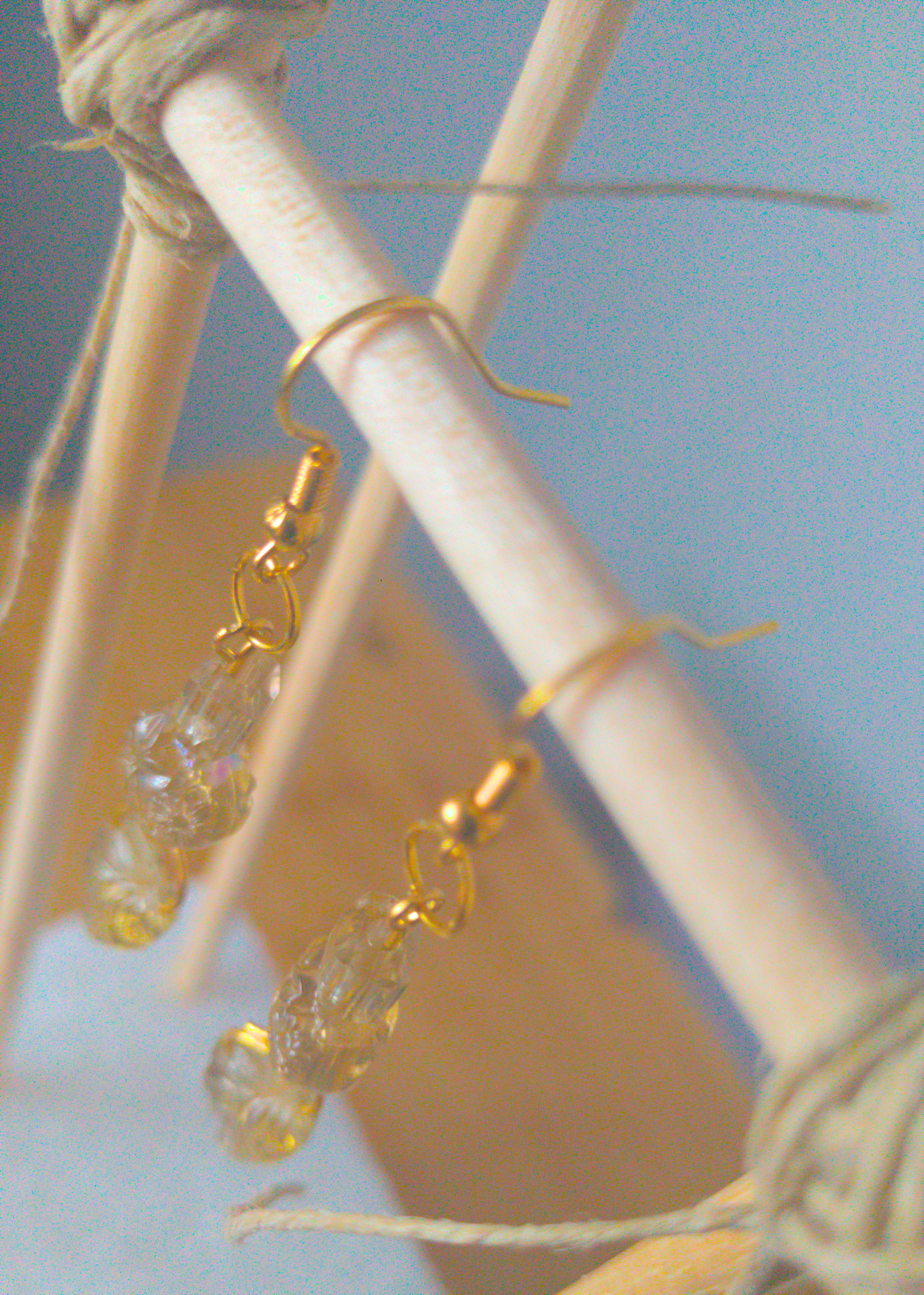 A top-down image of a pair of yellow handmade earrings being displayed on a stand. There three beads, one a square prism, one a circle with an imprint of a flower, one a leaf. They are all made of the same antique-colored plastic. The hooks are a golden color.