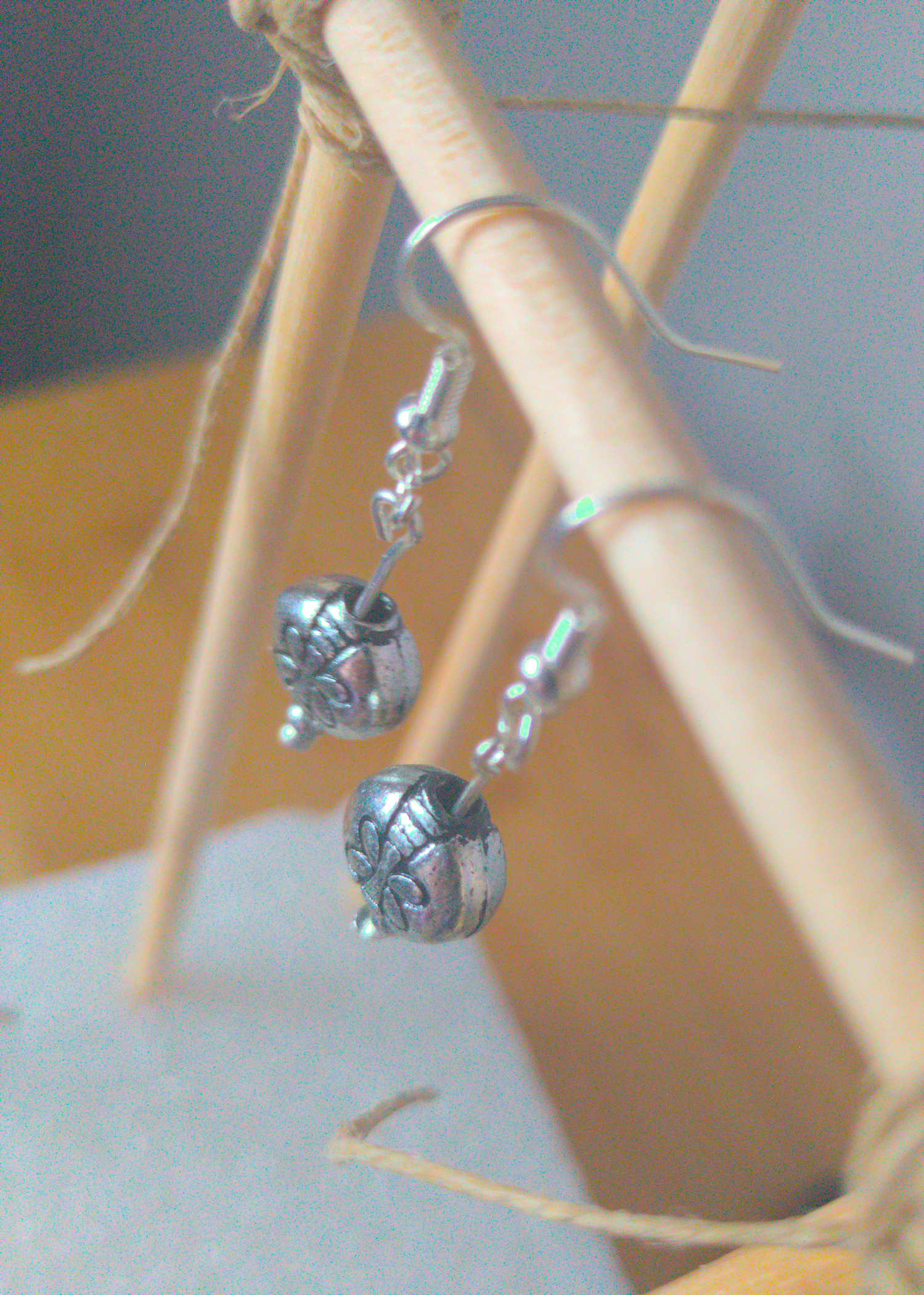 A top-down image of a pair of silver handmade earrings being displayed on a stand. There is a dragonfly motif on the round bead that is the focal piece of the earrings. The hooks are a silver color.