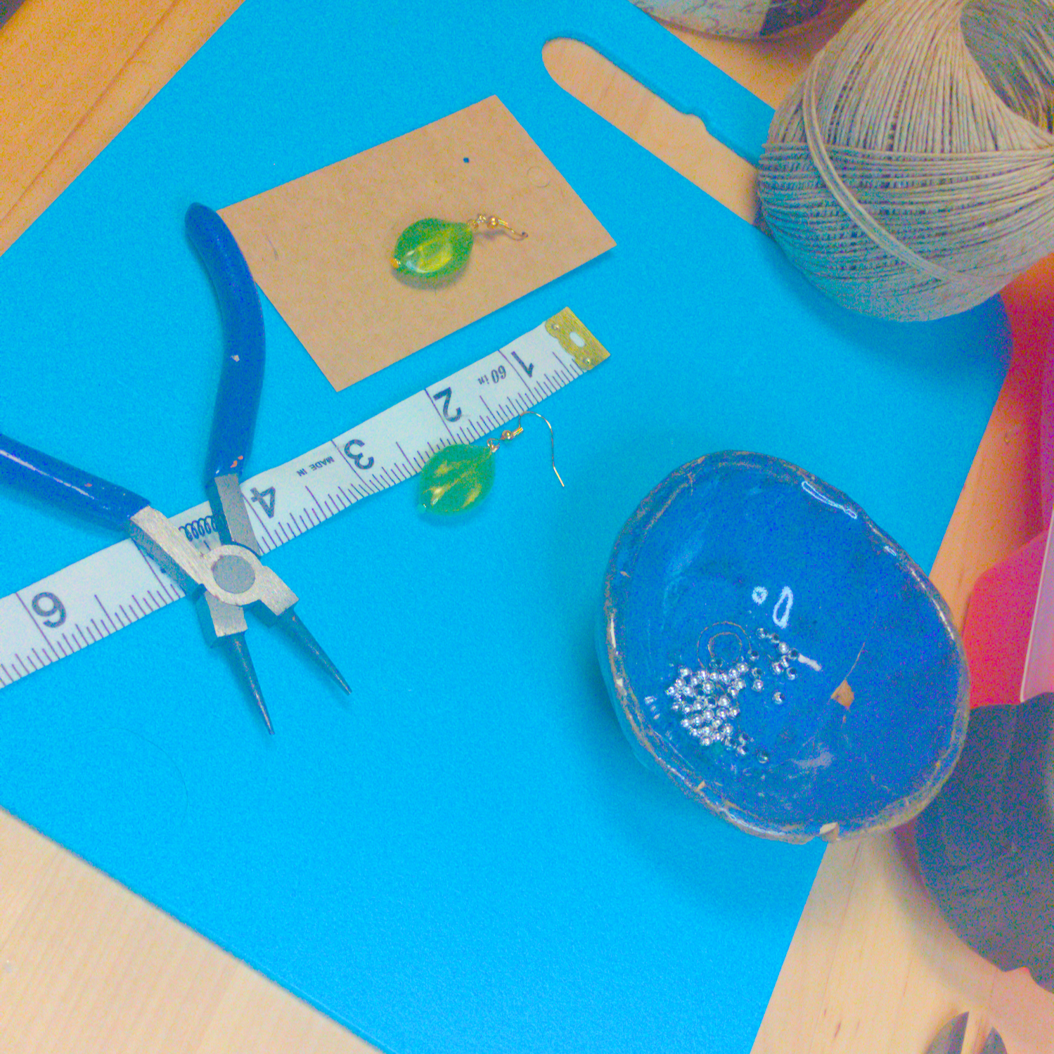 An image of a pair of green handmade earrings being measured on a work table. The pair is 1.75 inches long.