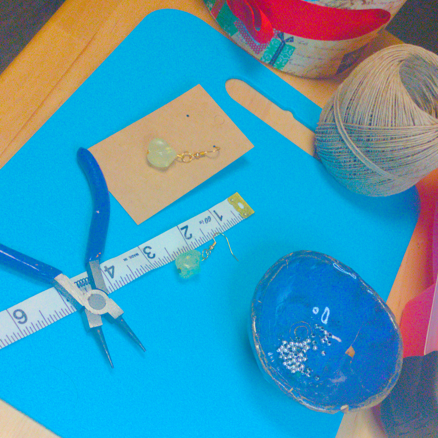 An image of a pair of green handmade earrings being measured on a work table. The pair is 1.5 inches long.