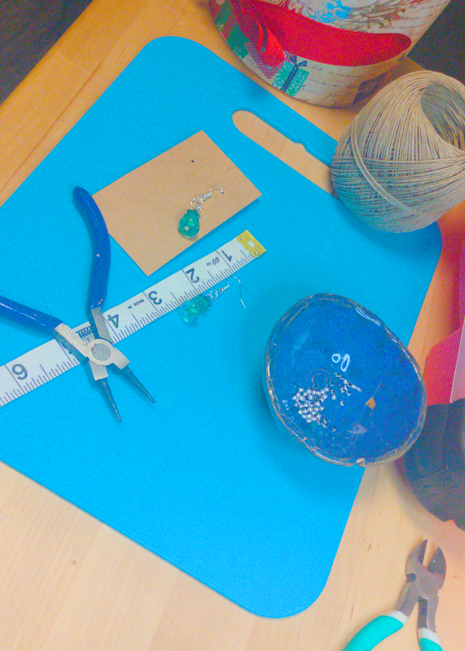 An image of a pair of green handmade earrings being measured on a work table. The pair is 1.5 inches long.