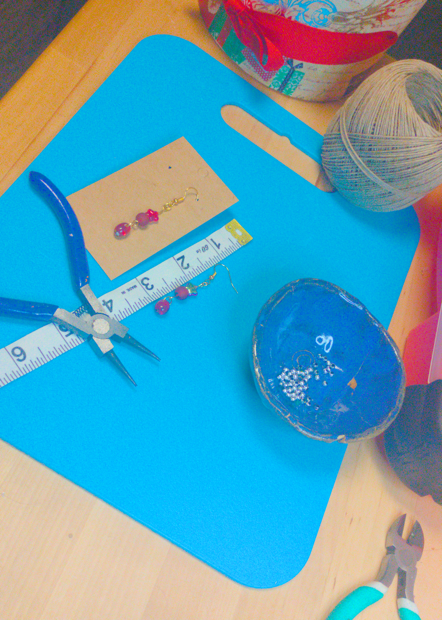 An image of a pair of red handmade earrings being measured on a work table. The pair is 2.25 inches long.