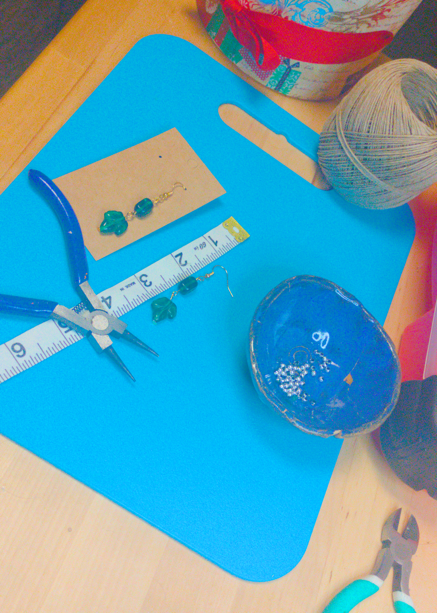 An image of a pair of green handmade earrings being measured on a work table. The pair is 2.5 inches long.