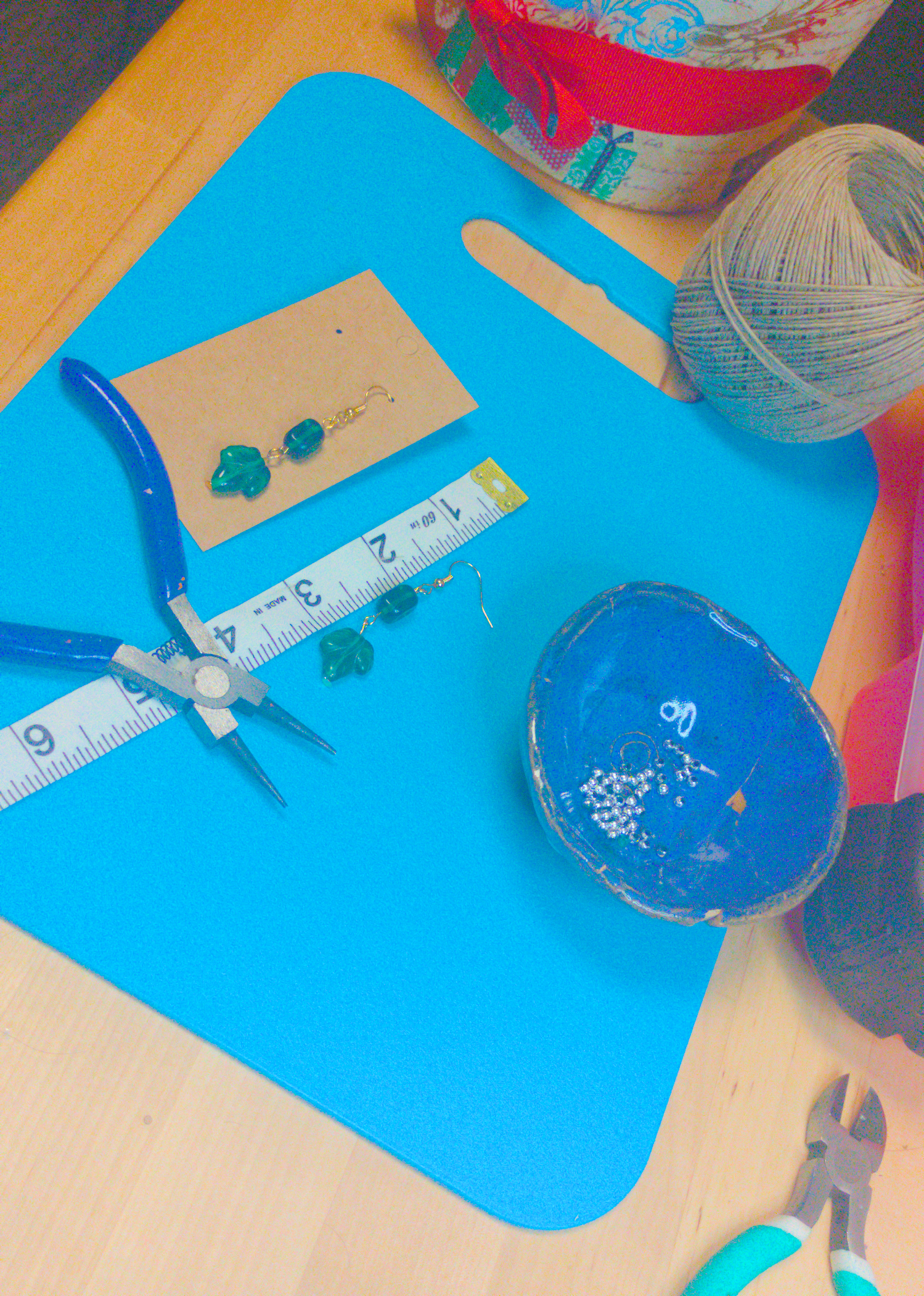 An image of a pair of green handmade earrings being measured on a work table. The pair is 2.5 inches long.
