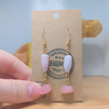A front facing image of a pair of handmade earrings. There is a thin, long, pink and white beads on top of a flat, triangular, pink bead. The hooks are golden.