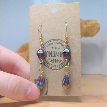 A front facing image of a pair of handmade earrings. There is a brown diamond shaped bead on top of a brown teardrop shaped bead. The hooks are a golden color.