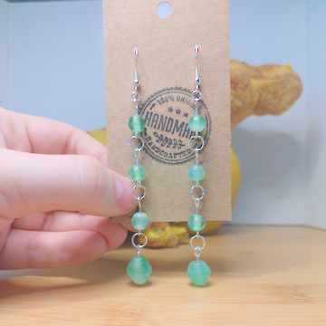 A front facing image of a pair of handmade earrings. There are four green beads that increase slightly in size down the earrings. The hooks are a silver color.