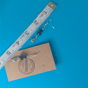 A pair of black and silver earrings being measured on a work table. The pair is 2 inches long.