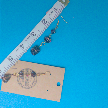A pair of black earrings being measured on a work table. The pair is 3 inches long.