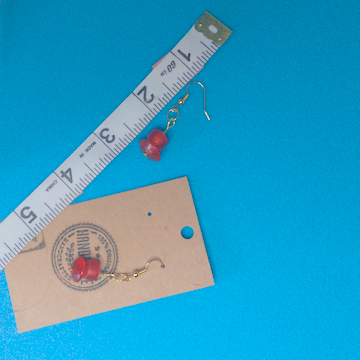 A pair of orange earrings being measured on a work table. The pair is 1.5 inches long.