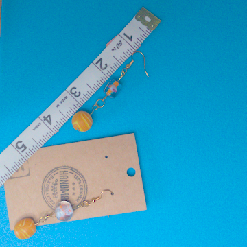 A pair of orange earrings being measured on a work table. The pair is 2.5 inches long.