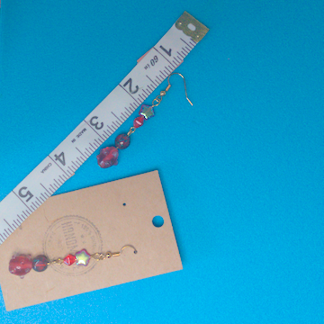 A pair of red earrings being measured on a work table. The pair is 2.5 inches long.