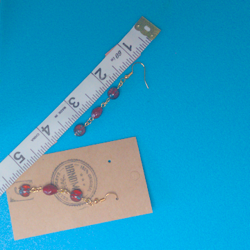 A pair of red earrings being measured on a work table. The pair is 2.5 inches long.