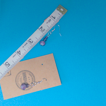 A pair of purple earrings being measured on a work table. The pair is 1.5 inches long.