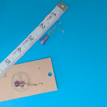 A pair of purple earrings being measured on a work table. The pair is 1.75 inches long.