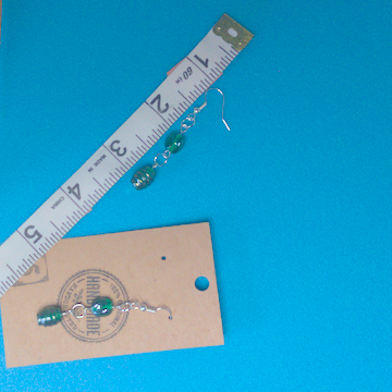 A pair of green earrings being measured on a work table. The pair is 2 inches long.