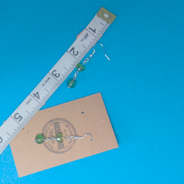 A pair of green earrings being measured on a work table. The pair is 2 inches long.