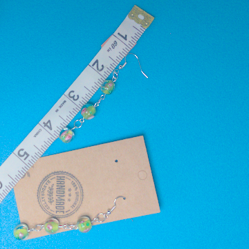 A pair of green earrings being measured on a work table. The pair is 3 inches long.