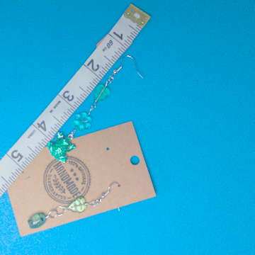 A pair of green earrings being measured on a work table. The longer earring is 3.25 inched long. The shorter one is 2.5 inches long.
