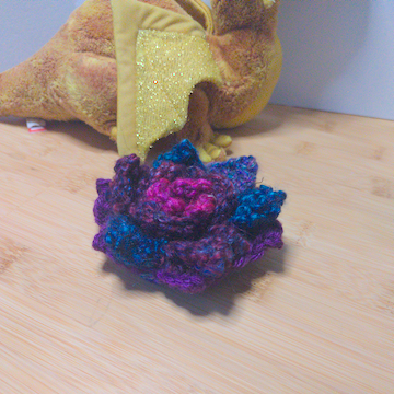 A blue and purple crochet flower with four layers of petals. The layers are stacked flat on top of each other.