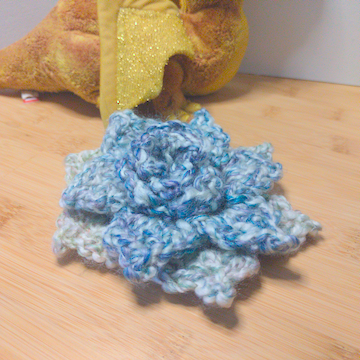 A white crochet flower with four layers of petals. The layers are stacked flat on top of each other.