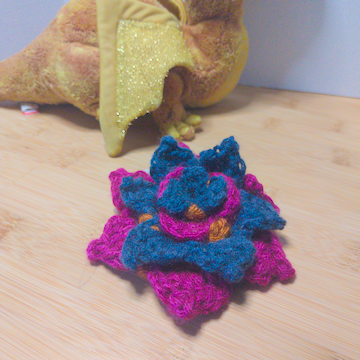 A blue and pink crochet flower with four layers of petals. The layers are stacked flat on top of each other.