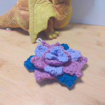 A purple, pink, and blue crochet flower with four layers of petals. The layers are stacked flat on top of each other.