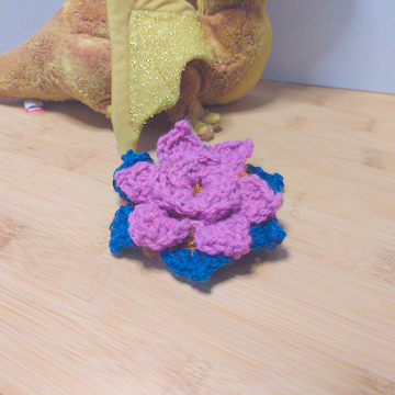 A pink and blue crochet flower with four layers of petals. The layers are stacked flat on top of each other.